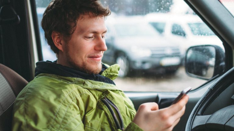 Eine Person sitzt mit dem Smartphone in der Hand in einem älteren Auto.