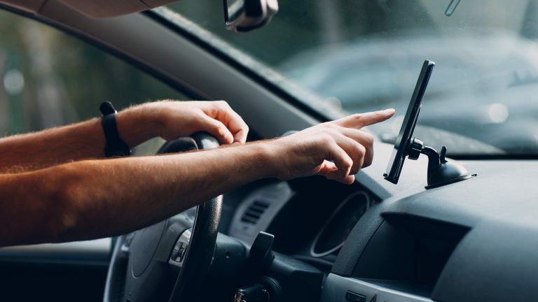 Eine Person tippt auf ein Handy, das in einer Halterung im Auto angebracht ist.