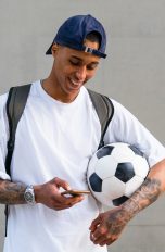 Eine Person mit einem Fußball unter dem Arm schaut auf ihr Smartphone.