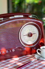 Ein altes Radio steht neben einer Kaffeetasse und einer Kaffeekanne auf einem kleinen Bistrotisch.