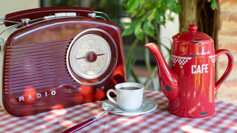 Ein altes Radio steht neben einer Kaffeetasse und einer Kaffeekanne auf einem kleinen Bistrotisch.