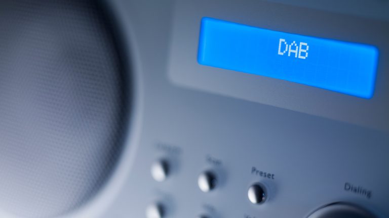 Ein kleiner blau leuchtender Bildschirm eines Digitalradios, auf dem DAB steht. 