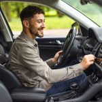 Eine Person sitzt im Fahrersitz eines Autos und stellt etwas an der Mittelkonsole ein.