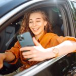 Eine Person sitzt in einem Auto und hält ein iPhone in der Hand.