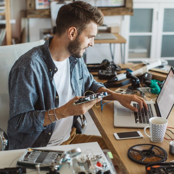 Eine Person sitzt an einem Tisch, auf dem zahlreiche Elektrokomponenten und Werkzeuge zu sehen sind.