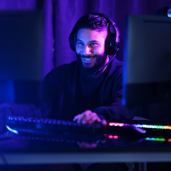 Eine Person mit Headset auf dem Kopf sitzt vor einem bunt leuchtenden Gaming-Setup.