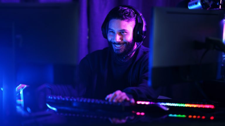 Eine Person mit Headset auf dem Kopf sitzt vor einem bunt leuchtenden Gaming-Setup.