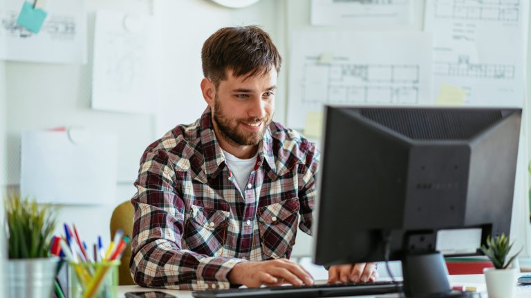 Eine Person sitzt lächelnd in einem Büro vor einem Rechner.