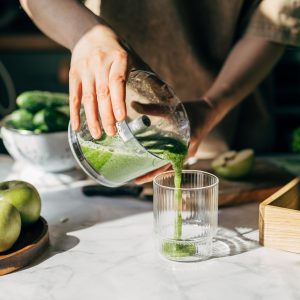 Eine Person gießt zerkleinertes Obst und Gemüse von einem Zerkleinerer in ein Glas.