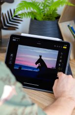 Eine Person sitzt vor einem iPad Air M2 mit angeheftetem Apple Pencil Pro und bearbeitet ein Foto über die Fotos-App.