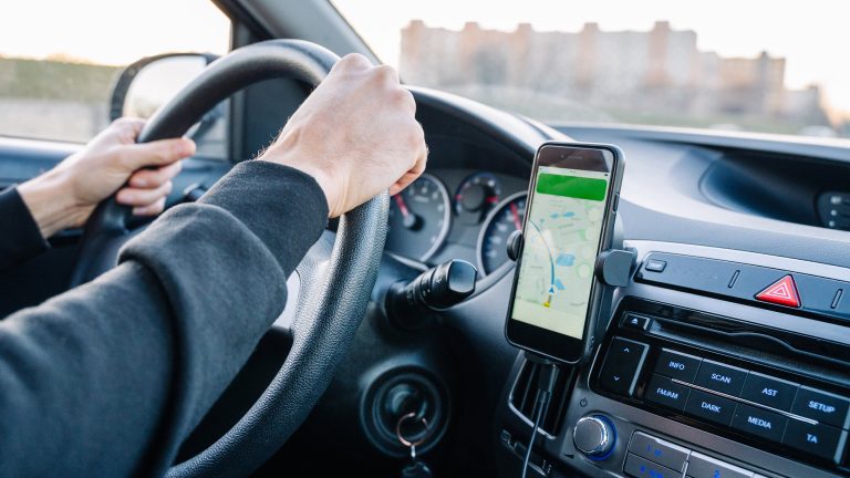 Eine Person fährt Auto. Am Lüftungsgitter ist ein Smartphone mit aktivierter Navigation angebracht.