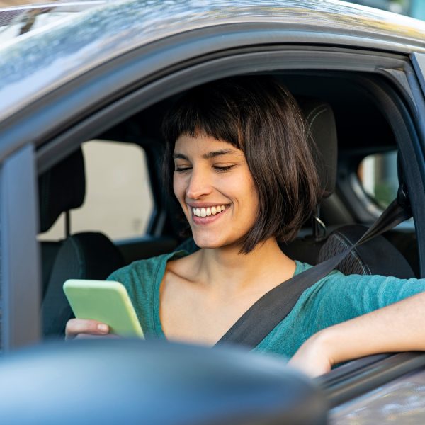 Eine Person sitzt in einem Auto und schaut auf ihr Smartphone.