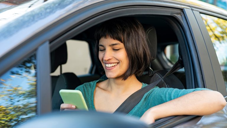 Eine Person sitzt in einem Auto und schaut auf ihr Smartphone.