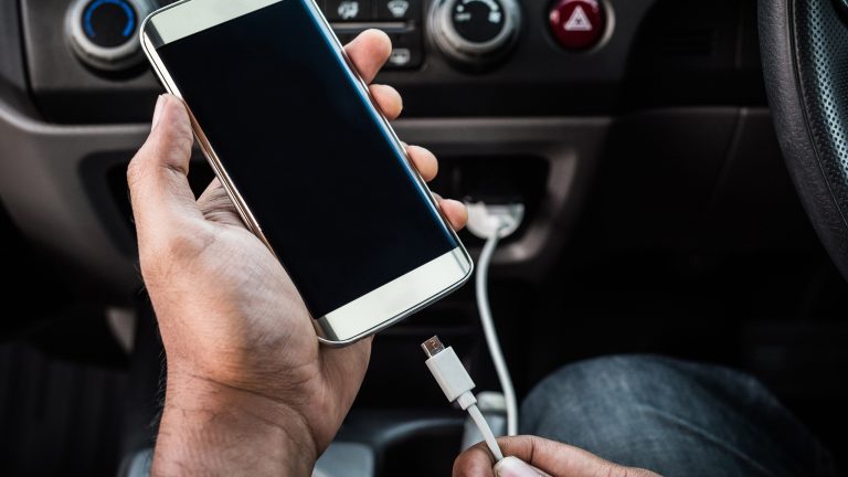 Eine Person steckt ein Smartphone an ein Kabel an, das ans Auto angeschlossen ist.