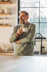 Eine Person steht mit einer Kaffeetasse angelehnt an der Küchentheke.