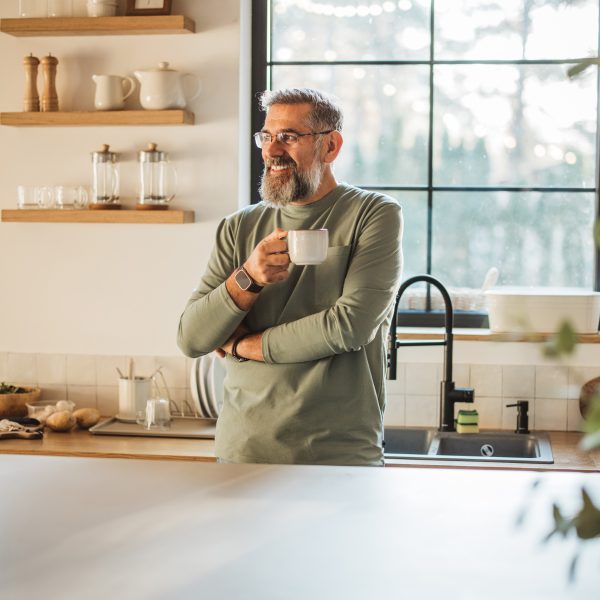 Eine Person steht mit einer Kaffeetasse angelehnt an der Küchentheke.