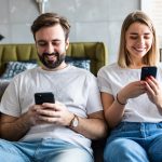 Zwei Personen sitzen nebeneinander auf einem Sofa und schauen in ihre Smartphones.