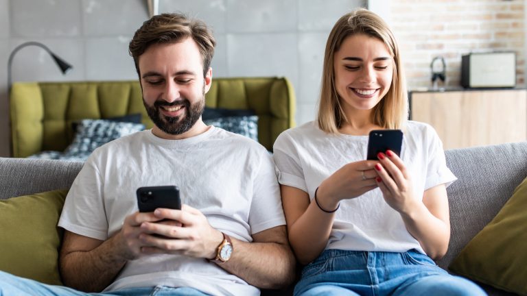 Zwei Personen sitzen nebeneinander auf einem Sofa und schauen in ihre Smartphones.