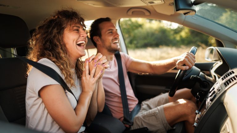 Zwei Personen sitzen in einem Auto und lachen während der Fahrt.