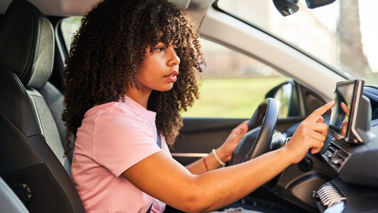 Eine Person sitzt ein einem Auto und bedient das Display von ihrem Infotainmentsystem.