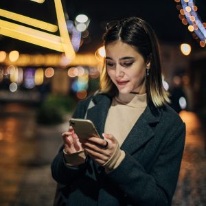 Eine Person steht nachts auf der Straße und blickt auf ihr Smartphone.