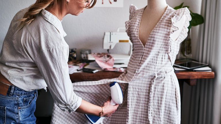 Eine Person nutzt eine Dampfbürste an einem Kleid auf einer Kleiderpuppe.