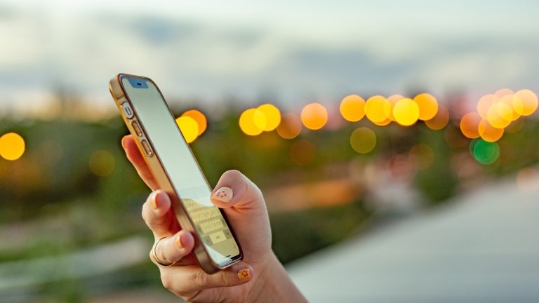 Eine Person hält ein Handy in der Hand und tippt darauf. Im Hintergrund sind viele Lichtpunkte. 