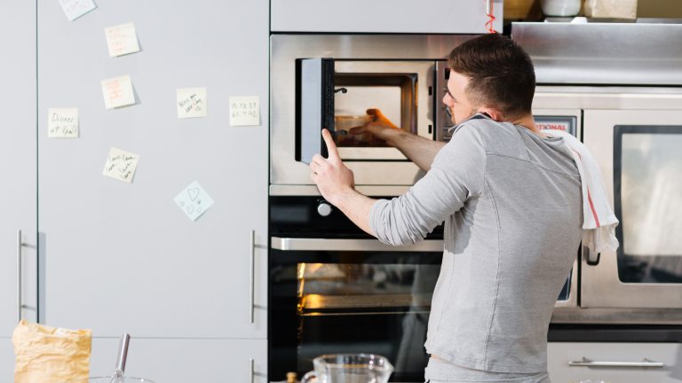 Eine Person stellt eine Schüssel mit Essen in die Mikrowelle während sie nebenbei telefoniert.