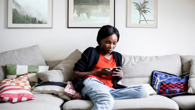 Eine Person sitzt auf dem Sofa und schaut auf ihr Smartphone.