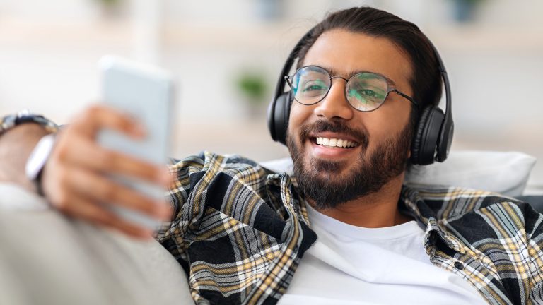 Eine Person sitzt mit Kopfhörern auf einer Couch und schaut auf ihr Smartphone.