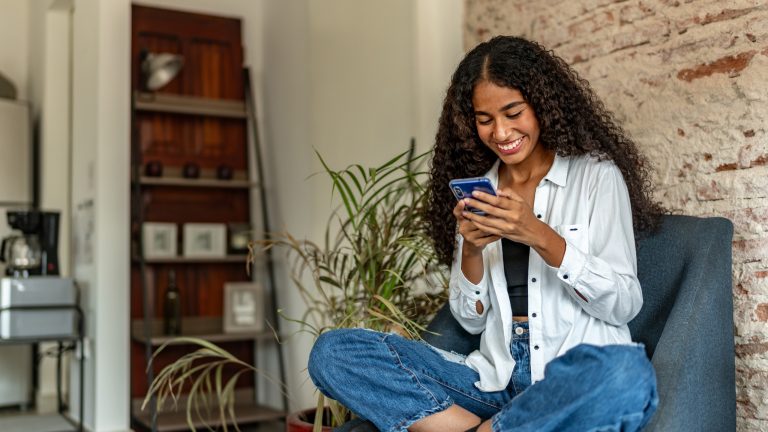 Eine Person sitzt im Schneidersitz auf einem Sessel und schaut auf ihr Smartphone.