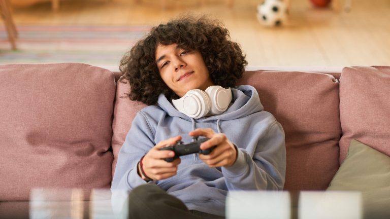 Eine Person sitzt auf einem Sofa und hält einen Controller in der Hand.