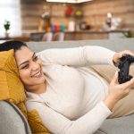 Eine Person liegt gemütlich auf einem Sofa und hält einen Controller in der Hand.