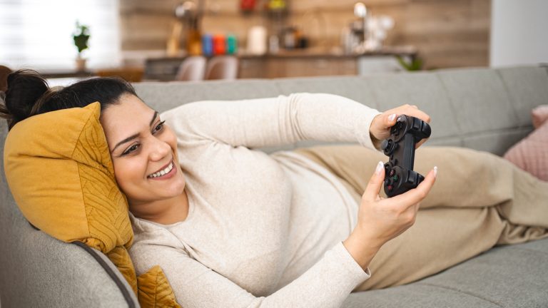 Eine Person liegt gemütlich auf einem Sofa und hält einen Controller in der Hand.