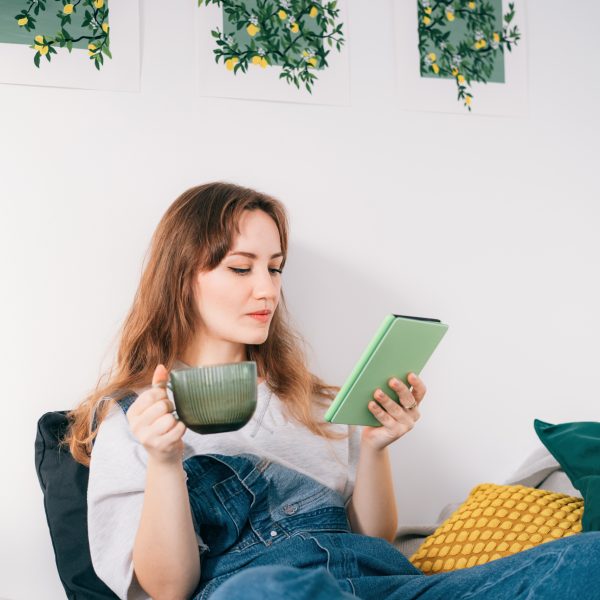 Eine Person hält eine Tasse in der Hand, während sie auf einem E Book-Reader liest.