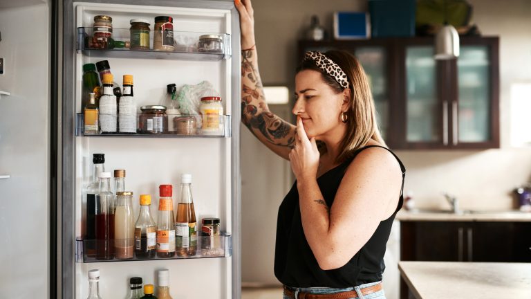 Eine Person steht grübelnd vor einem geöffneten Kühlschrank.