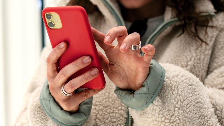 Eine Person hält im Freien ein Smartphone mit einer Schutzhülle in der Hand und tippt.