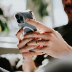 Ein iPhone in den Händen einer Person, die auf einer Couch vor einem Fenster sitzt.