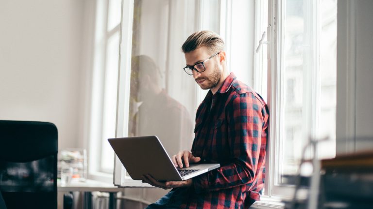 Eine Person lehnt an einem Fenster und hält einen Laptop in der Hand.