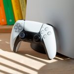 Bild einer PS5 mitsamt Dualsense-Controller, die im Sonnenlicht auf einem Holzboden steht.