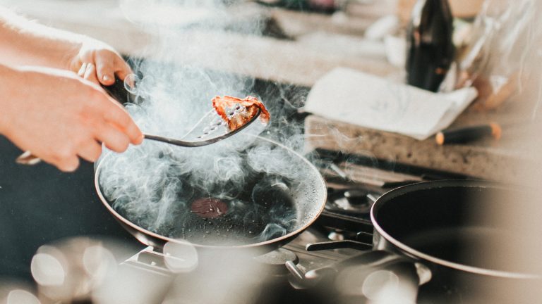 In einer dampfenden Pfanne wird ein Stück Bacon gebraten.