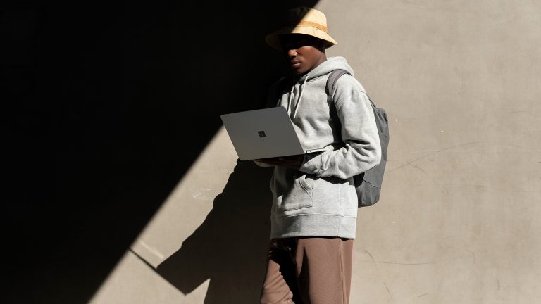 Eine Person lehnt an einer Wand und schaut in einen aufgeklappten Laptop.