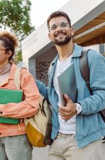 Zwei Personen entfernen sich von der Uni und tragen Arbeitsmaterial in den Händen.