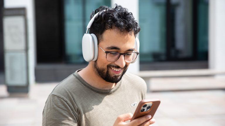 Eine Person hält ein iPhone in der Hand und hat AirPods Max auf dem Kopf.