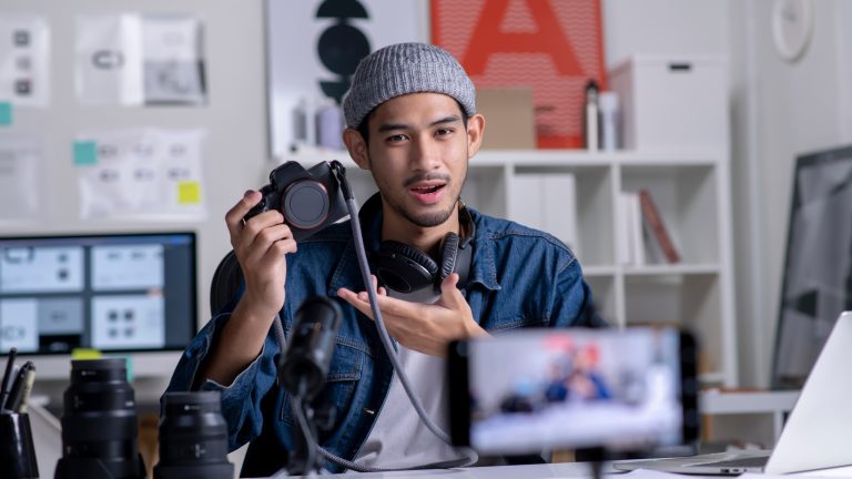 Eine Person hält eine Kamera in der Hand und filmt sich mit einem Smartphone.