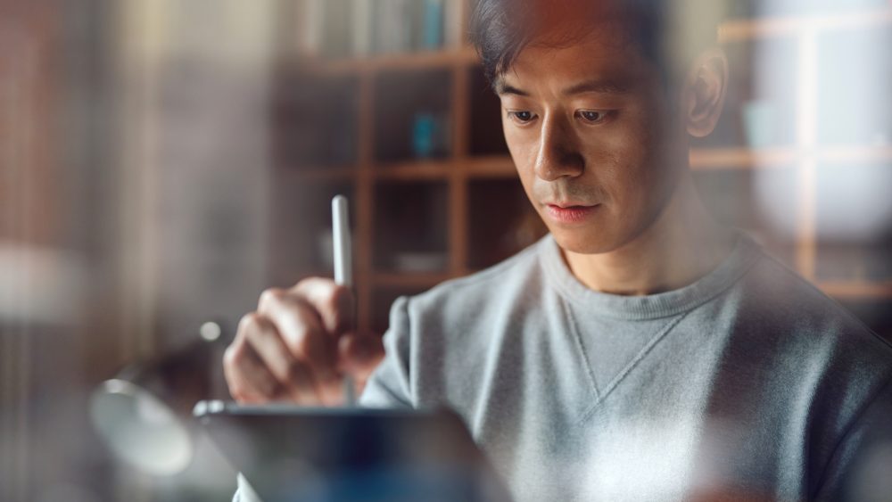 Eine Person hält einen Apple Pencil in der Hand und scheint etwas auf einem Display zu zeichnen.