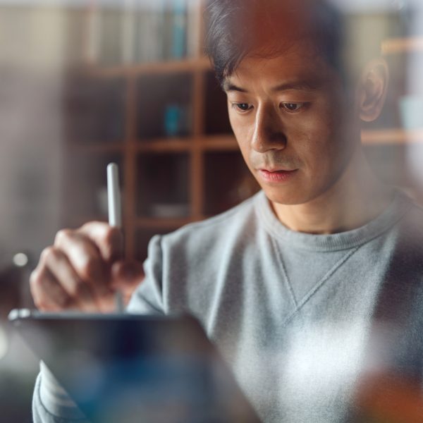 Eine Person hält einen Apple Pencil in der Hand und scheint etwas auf einem Display zu zeichnen.