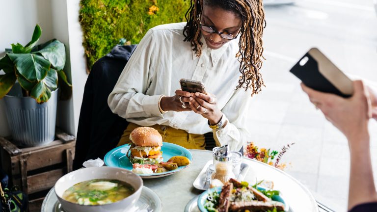 Eine Person schießt mit ihrem Smartphone ein Foto von einem Burger im Restaurant.