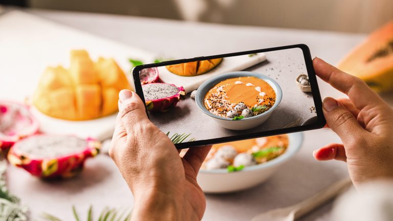 Nahaufnahme der Hände einer Person, die mit dem Smartphone ein Foto einer herbstlichen Bowl schießt.