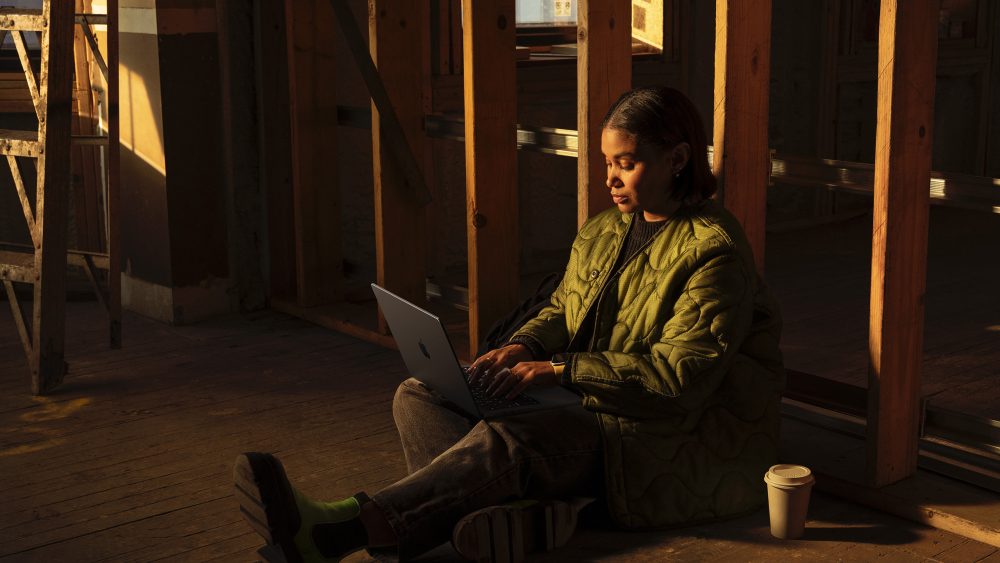 Eine Person sitzt mit einem Laptop auf dem Schoß am Boden eines Raumes, der gerade renoviert wird.